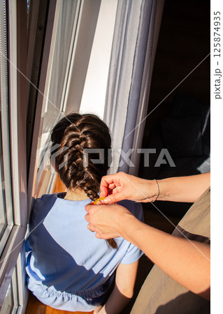 Woman braiding her daughter's hair. Mother and daughter enjoying quiet intimate moment Precise braiding process shown in detail. 125874935