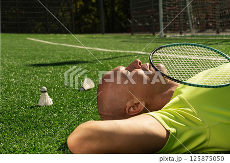 Badminton player resting after game, lying and enjoy on sport court with green grass. Outdoors. Summer sports game. Copy space. Close up. Badminton player resting after game, lying and enjoy on sport court with green grass. Outdoors. Summer sports game. Copy space. Close up. 125875050