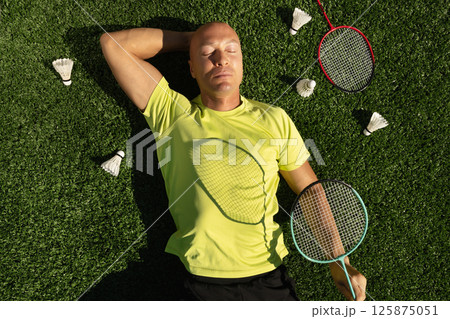 Badminton player resting after game, lying and enjoy on sport court in public park with artificial turf as green grass. Outdoors. Creative. Summer relax. View from above Badminton player resting after game, lying and enjoy on sport court in public park with artificial turf as green grass. Outdoors. Creative. Summer relax. View from above 125875051