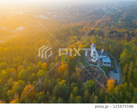 The Liberecka Vysina lookout tower stands amidst vibrant autumn foliage, bathed in warm sunset light. Surrounding hills offer a picturesque backdrop to this scenic landmark in Liberec, Czechia. The Liberecka Vysina lookout tower stands amidst vibrant autumn foliage, bathed in warm sunset light. Surrounding hills offer a picturesque backdrop to this scenic landmark in Liberec, Czechia. 125875596