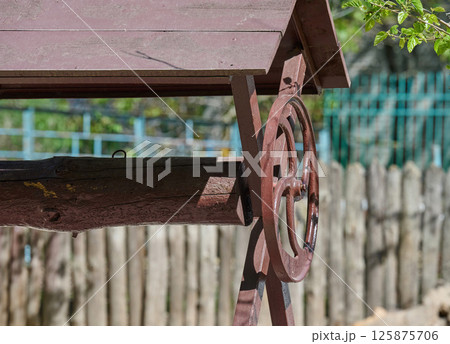 Vintage wooden water well with a hand crank and weathered roof, set against a rustic wooden fence and garden background Vintage wooden water well with a hand crank and weathered roof, set against a rustic wooden fence and garden background 125875706