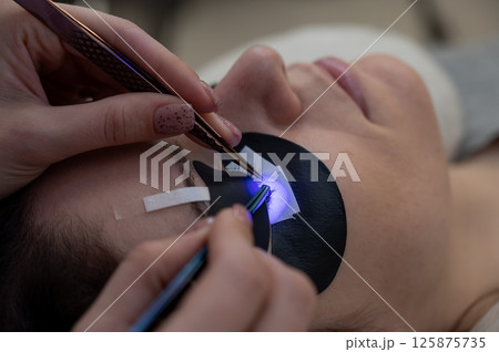 A woman undergoing eyelash extension procedure using an ultraviolet lamp. 125875735