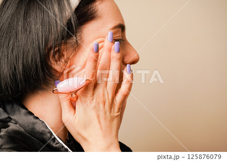 Caring for aging skin. Applying cream to face. Woman in black pajamas and with a headband doing beauty procedures at home. Girl doing facial massage with her hands. Caring for aging skin. Applying cream to face. Woman in black pajamas and with a headband doing beauty procedures at home. Girl doing facial massage with her hands. 125876079