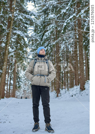 Winter Wonderland Adventure Young Man Hiking Snow Covered Forest Path Surrounded by Towering Pine Trees Serene Nature Exploration Scene Capturing Outdoor Enthusiast in Cozy Cold Weather Gear 125876085