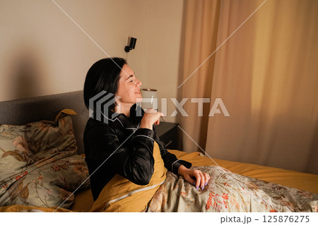 Starting her day, a woman yawns after waking up. Her cheerful expression emphasizes a fresh and relaxed start. Floral bedding adds charm. Starting her day, a woman yawns after waking up. Her cheerful expression emphasizes a fresh and relaxed start. Floral bedding adds charm. 125876275