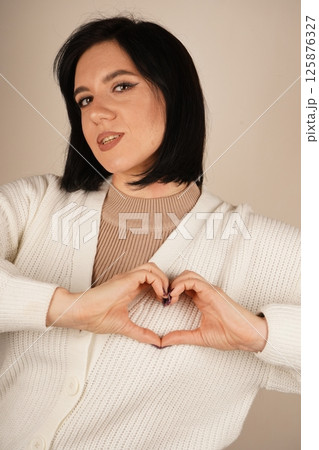 Her calm demeanor reflects a sincere moment. A beautiful display of love. Smiling calmly, the woman forms her hands into a heart, which embodies love and peace. 125876327