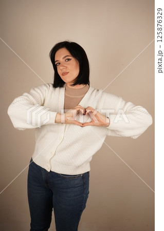 A moment filled with love and positivity. The young woman forms a heart shape with her hands, radiating warmth and affection. Her gentle smile enhances the serene and relaxed pose. 125876329