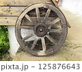 An old wooden cart wheel stands on a concrete path against a background of planks. Transportation used in villages, ranches, and farms. Vintage and antique 125876643