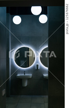 Modern public toilet hall interior with white sinks and round mirror. Nobody inside 125876662