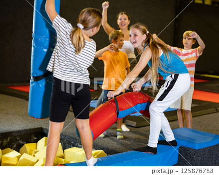 Teen girl doing funny fighting on battle beam with preteen girl 125876788