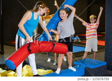Tween girl fighting by pugil stick with female friend on inflatable beam Tween girl fighting by pugil stick with female friend on inflatable beam 125876789