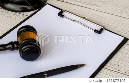 Side view of blank white paper clipboard with customizable space for text and with gavel next to it. Copy space concept. Side view of blank white paper clipboard with customizable space for text and with gavel next to it. Copy space concept. 125877105