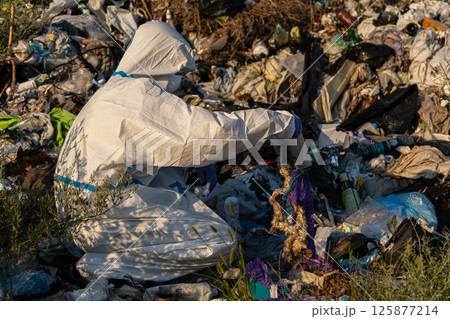 An environmental worker in protective gear is sorting through trash in a landfill during sunset, aiming to clean up plastic waste An environmental worker in protective gear is sorting through trash in a landfill during sunset, aiming to clean up plastic waste 125877214