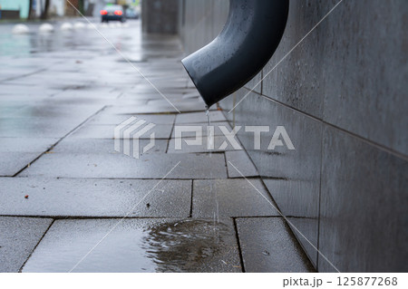 Water drips from a drain pipe onto slick pavement, showing the aftermath of rain in an urban environment Water drips from a drain pipe onto slick pavement, showing the aftermath of rain in an urban environment 125877268