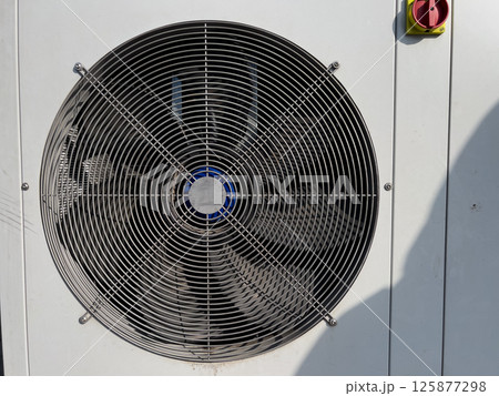 Large metal fan spins rapidly, providing ventilation for equipment outside a building construction site on a sunny day Large metal fan spins rapidly, providing ventilation for equipment outside a building construction site on a sunny day 125877298