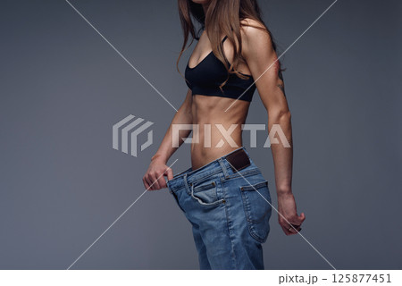 Woman with perfect body demonstrates weight loss, slimming by wearing old big jeans Woman with perfect body demonstrates weight loss, slimming by wearing old big jeans 125877451