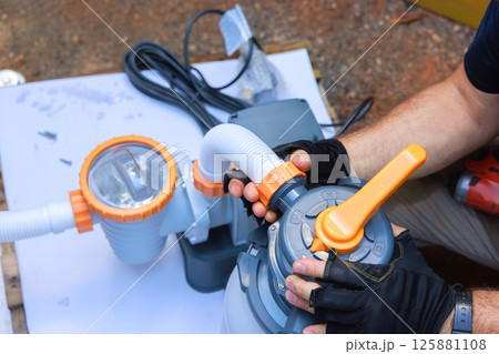 Contractor attaches components of swimming pool pump system on outdoors near swimming pool 125881108