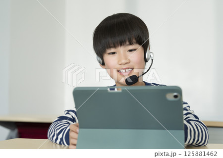 ヘッドセットをつけてタブレットPCに向かう小学4年生の男の子 ヘッドセットをつけてタブレットPCに向かう小学4年生の男の子 125881462