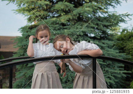 Schoolgirls in identical outfits look like an illustration from a children's book. The snail on the railing becomes the center of their world for a moment. Schoolgirls in identical outfits look like an illustration from a children's book. The snail on the railing becomes the center of their world for a moment. 125881935