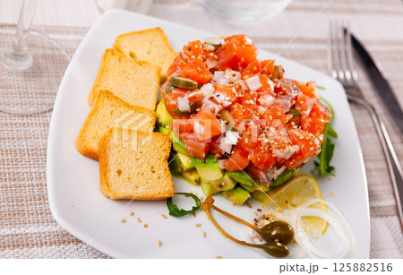 Salmon tartare with avocado served with toasts, arugula, lemon and capers Salmon tartare with avocado served with toasts, arugula, lemon and capers 125882516