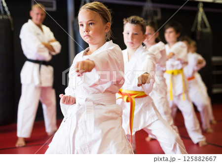 Kids in kimonos practicing karate techniques in group workout at training room Kids in kimonos practicing karate techniques in group workout at training room 125882667