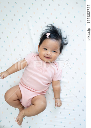 Joyful newborn baby smiling in pink outfit asian infant indoor setting close-up perspective 125882725