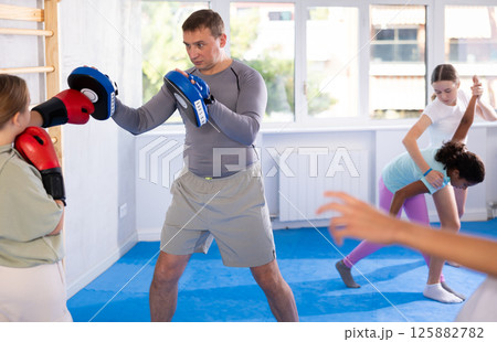 Focused girl hitting the focus mitts held by his boxing trainer in gym Focused girl hitting the focus mitts held by his boxing trainer in gym 125882782
