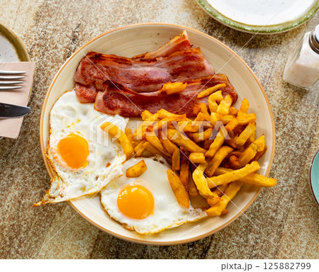 Fried eggs with sliced bacon and french fries Fried eggs with sliced bacon and french fries 125882799