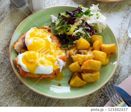Eggs Benedict with smoked salmon, fried potatoes and greens 125882837