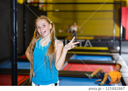 Portrait of excited teenage girl in sportswear posing and smiling at camera on colorful trampoline at game club 125882867