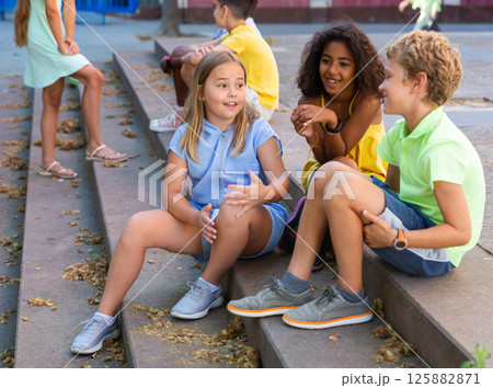 Children talking together while sitting on stairs outdoors Children talking together while sitting on stairs outdoors 125882871