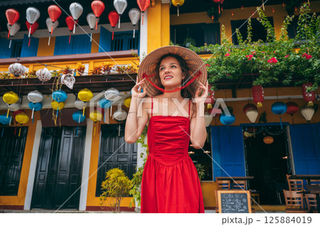 portrait of happy beautiful female tourist in traditional Vietnamese hat on the street in Hoi An city in Vietnam in Asia 125884019