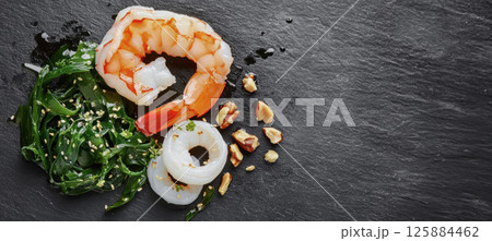 Macro shot salad: a juicy shrimp with a glossy dressing, a curled slice of calamari, and a few strands of wakame resting alongside a sprinkle of chopped nuts Macro shot salad: a juicy shrimp with a glossy dressing, a curled slice of calamari, and a few strands of wakame resting alongside a sprinkle of chopped nuts 125884462