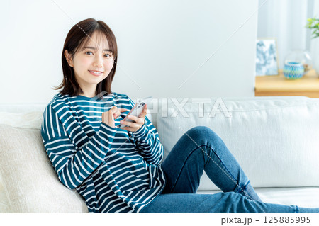 部屋でスマホを操作する若い女性 125885995