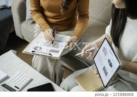 Two professionals reviewing financial charts on a tablet and clipboard during a business meeting in a modern office environment. Two professionals reviewing financial charts on a tablet and clipboard during a business meeting in a modern office environment. 125886008