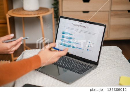 Professionals reviewing data on a laptop, focusing on graphs and charts, in a modern office environment. 125886012