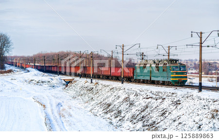 Freight train hauled by an electric locomotive in winter in Kyiv Oblast of Ukraine 125889863