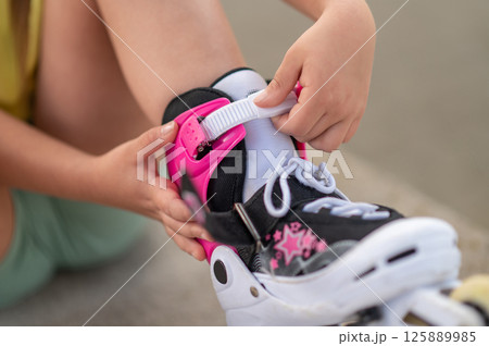 Unrecognizable female kid putting on roller-skates fastening buckles preparing for active skating 125889985