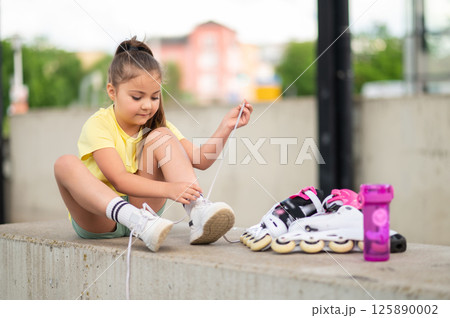 Little girl wearing roller-skates preparing for outdoor skating Little girl wearing roller-skates preparing for outdoor skating 125890002