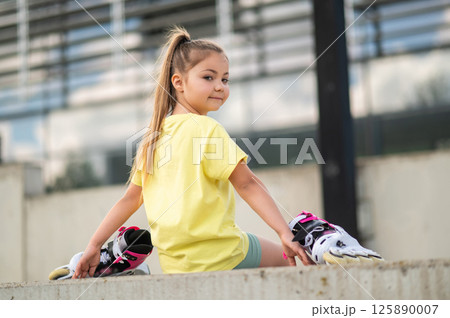 Energetic female child holding roller-skates playing outside 125890007
