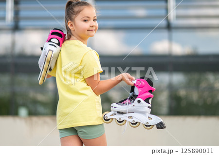 Energetic female child holding roller-skates playing outside Energetic female child holding roller-skates playing outside 125890011