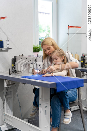 Mom and daughter sitting together at the sewing machine and looking busy Mom and daughter sitting together at the sewing machine and looking busy 125890099