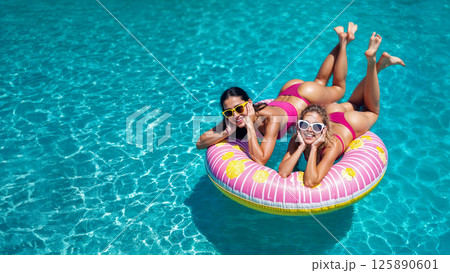 Young women in early twenties on pink inflatable pool ring floating on water. Space for text 125890601