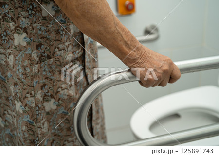 Asian elderly woman patient use toilet support rail in bathroom. Asian elderly woman patient use toilet support rail in bathroom. 125891743