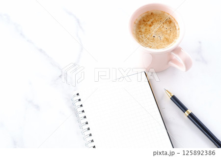 コーヒーを飲みながら、リング式のメモ帳とペンでデスクワークをしているイメージ コーヒーを飲みながら、リング式のメモ帳とペンでデスクワークをしているイメージ 125892386