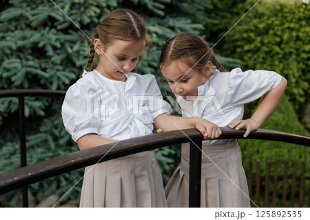 The twins carefully examine the snail crawling along the wooden surface. The girls with two braids look sweet and harmonious. 125892535