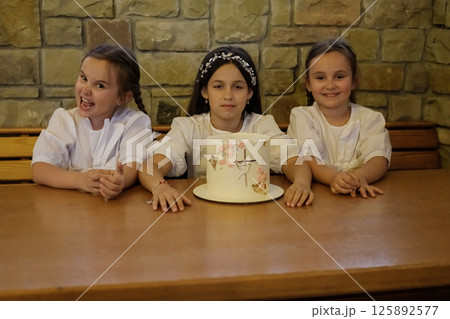 The twin girls and the older girl celebrate together at the table. The cake is decorated with great love, as seen in the girls' eyes. The twin girls and the older girl celebrate together at the table. The cake is decorated with great love, as seen in the girls' eyes. 125892577