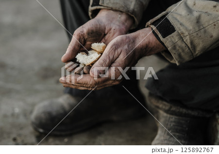 The aged hands grip the bread with quiet desperation. The hands bear the weight of a lifetime of work. 125892767