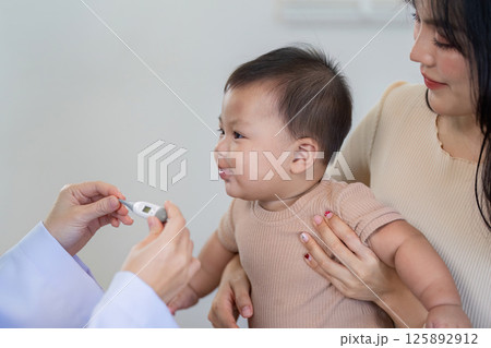 Baby reacting to temperature measurement by pediatrician in clinic. 125892912