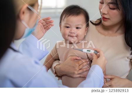 Pediatrician checking baby temperature with thermometer in clinic. Pediatrician checking baby temperature with thermometer in clinic. 125892913